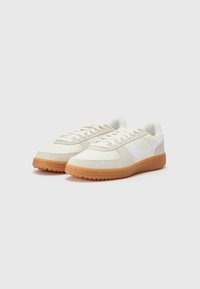 Baskets blanches avec une tige texturée, dotées d'un logo swoosh blanc et d'une semelle en caoutchouc naturel. Les lacets et le col rembourré complètent le design.
