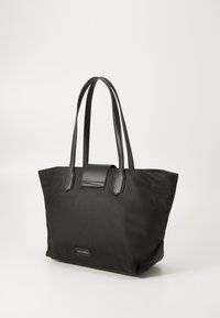 Black nylon tote bag with leather handles, structured shape, and a front flap detail. Minimalist design featuring a logo accent at the base.