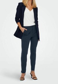 Marina skräddarsydda byxor med slim fit, sidofickor och en mjuk tygstruktur. Matchas med en vit topp med vågformad kant och svarta klacksandaler.