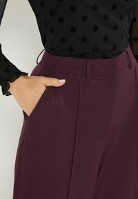 Bordeaux op maat gemaakte broek met een gladde textuur, voorzien van zijzakken en een rechte pasvorm, gecombineerd met een zwart met witte stippen top.
