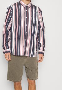 Langarm, knoopsluiting overhemd met verticale strepen in marineblauw, wit en rood. Voorzien van een kraag en een borstzak. De stof lijkt glad te zijn.