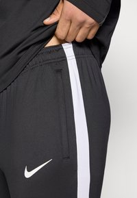 Μαύρο αθλητικό παντελόνι με λευκή πλευρική ρίγα, με ελαστική μέση και μικρό λογότυπο Nike στον μηρό. Μαλακό, ελαστικό ύφασμα.