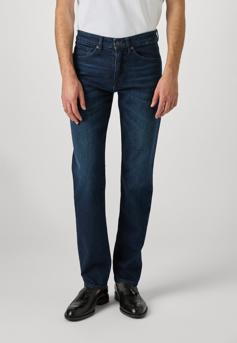 Jeans de denim azul oscuro con corte recto, diseño de cinco bolsillos y cierre de botón. La tela tiene una textura suave y un ligero desvanecimiento.