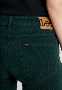 Mörkgrön kordflorsbyxor med ribbad textur. Har en läderetikett med "Lee" och en liten tygetikett på fickan.