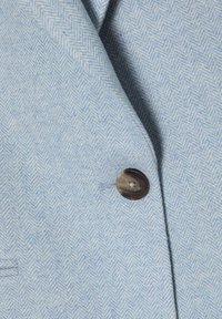 Tissu en chevron bleu clair avec un seul gros bouton foncé cousu et une petite poche fendue visible sur le côté.