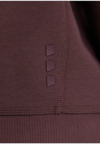 Top athletico bordeaux con finitura strutturata, orlo a costine e tre dettagli in gomma lungo la cucitura laterale. Cuciture visibili.