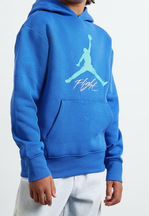 Person iført en blå hættetrøje med en teal silhuet af en springende basketballspiller og ordet "Flight" i hvid skrift.