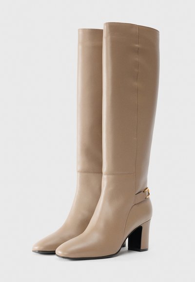 Knee-high beige leather boots with a pointed toe, a chunky heel, and a decorative buckle on the side. Smooth texture and clean stitching.