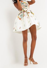 Blommigt mönsterklänning med en åtsittande bodice och utsvängd kjol. Vit botten, flerfärgade blommor och en rosett vid midjan. Guldiga klackar.