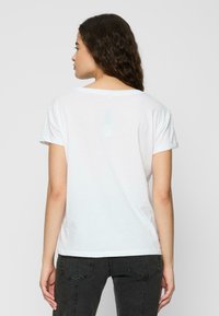White cotton t-shirt with short sleeves, round neckline, and a relaxed fit. Textured fabric with minimal details, worn with dark gray pants.