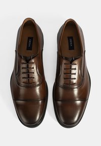 Bruine leren schoenen met een gladde afwerking, voorzien van een vetersluiting, ronde neus en subtiele stiksels langs de randen.