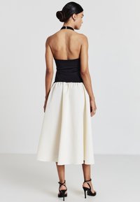 Top nero senza spalline abbinato a una gonna bianca al ginocchio con vita arricciata. Sandali neri con tacco alto completano il look.