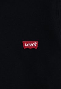 Black fabric with a small, red, embroidered Levi's logo patch featuring white lettering. The texture appears smooth and uniform.