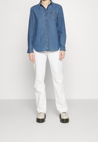 Jeansskjorta med långa ärmar, knäppning och bröstficka, tillsammans med vita raka byxor och beige skor med svarta sulor.