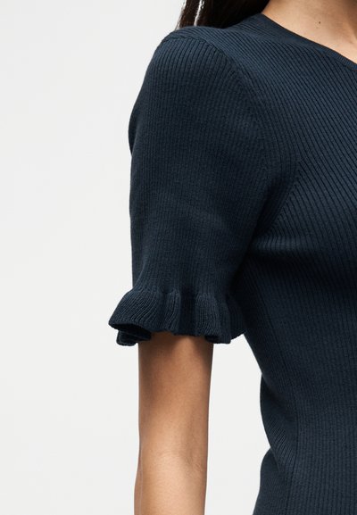 Μπλε ναυτικό ριμπ πλεκτό τοπ με κοντά μανίκια με βολάν στο τελείωμα, δομημένο λαιμόκοψη και εφαρμοστή γραμμή. Φαίνεται λεπτομέρεια υφής υφάσματος.