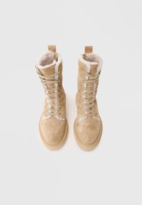 Bottes en suède beige à lacets avec des garnitures en fausse fourrure, bout arrondi et semelle en caoutchouc épaisse. Présente des accentuations cousues et une languette sur la tige.
