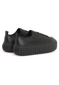 Zapatillas de cuero negro con una suela de plataforma texturizada, presentando punteras redondeadas, superficie lisa y cordones en tonos similares.