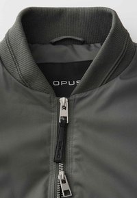 Dark gray jacket collar with ribbed fabric and dual silver zippers, one featuring a black pull tab with the brand name "Opus" visible inside.