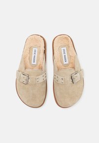 Bežové semišové klzáky s nastaviteľnými prackami a plyšovým kožúškom, ploché hnedé podrážky, označené Steve Madden vo vnútri.