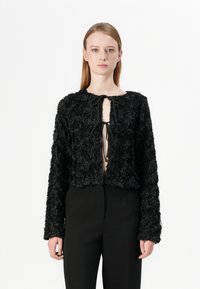 Veste noire en tissu floral texturé avec de longues manches et un col rond. Elle dispose d'une fermeture à lien sur le devant et d'un design court.