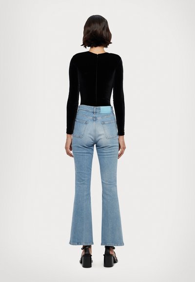 Svart langermet bodysuit parret med lys blå utsvungne jeans med en blå etikett i livet og baklommer. Svart blokkhælt sandaler.