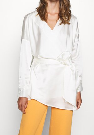 Top avvolgente bianco in satin con maniche lunghe e vita legata, abbinato a pantaloni gialli a gamba larga. Tessuto morbido e scollatura a V.