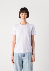 Lilla t-skjorte i bomull med rund hals og korte ermer. Har en subtil logo på brystet og en avslappet passform. Kombinert med lyseblå jeans.