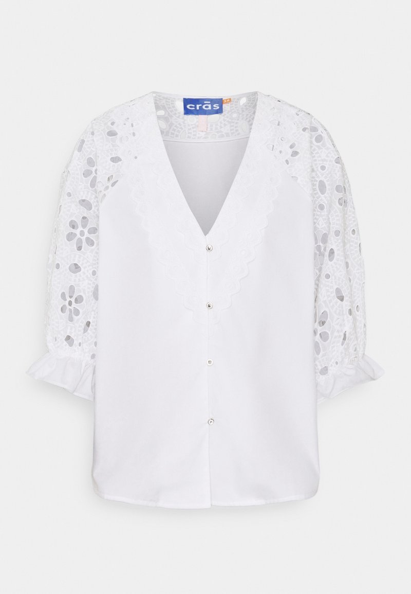 Blusa bianca con scollatura a V profonda e chiusura con bottoni. Presenta elaborati maniche a sbuffo in pizzo e dettagli di colletto ondulato.