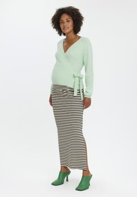 Mintgrøn indpakningsstriktrøje i blødt strik, parret med en sort og beige stribet pencil skirt. Afsluttet med grønne højhælede sko.