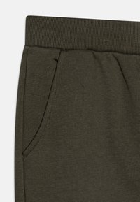 Mörk olivgrön sweatshirtbyxor med en ribbad midja, som har en sidficka och är tillverkade av ett mjukt, texturerat tyg.