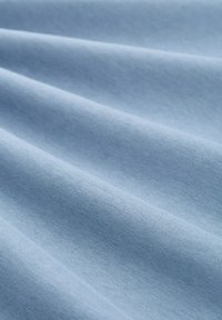 Světle modrá tkanina s jemnými sklady a hladkou, jemnou strukturou, rovnoměrně osvětlená, aby vyzdvihla tkaní materiálu.