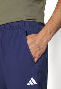 Navy athletic shorts with a zippered pocket and elastic waistband. Features a white logo on the left side and textured fabric.