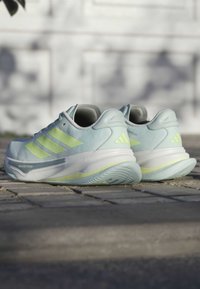 Baskets de sport bleu clair avec des accents vert fluo, tige en maille, semelle texturée et logo à trois bandes sur le côté.