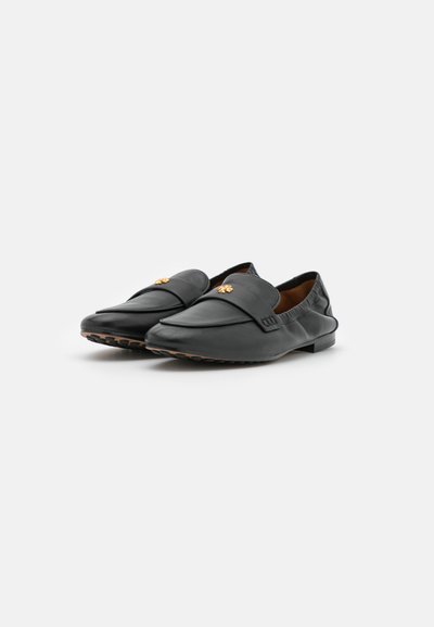 Mocassins en cuir noir avec une finition lisse, présentant un emblème en relief sur le dessus et un design minimaliste. Semelle en caoutchouc pour une meilleure adhérence.