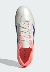 Botín de fútbol con parte superior sintética blanca, acentos rosas, logotipos azules y superficie texturizada. Incluye cordones tradicionales y una suela acolchada.