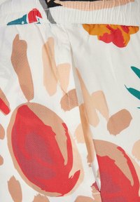 Tela blanca con patrones abstractos florales y de hojas en rojo, beige y naranja, con costuras visibles y pliegues.