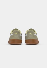 Baskets de sport en daim vert avec une semelle en caoutchouc beige, des accents blancs et un logo jaune sur le talon. Présente un design bas.