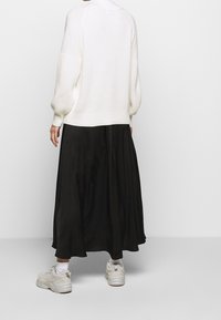Pull en tricot blanc avec des manches bouffantes, associé à une jupe noire fluide. Chaussures comprenant des baskets de couleur claire et des chaussettes blanches visibles.