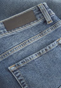 Zilas džinsa bikses ar ādas etiķeti ar uzrakstu "GABBA", šūtu aizmugurē. Redzamas šuves un klasiskas griezums ar kabatas detaļām.