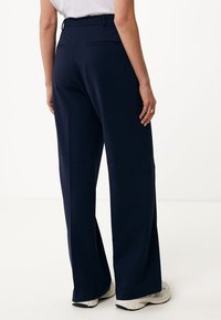 Marineblauwe wijde broek met een gladde textuur, twee achterzakken en een getailleerde pasvorm, gecombineerd met lichtgekleurde schoenen.