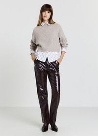 Maglione beige chiaro a maglia cable sovrapposto a una camicia bianca a righe, abbinato a pantaloni bordeaux scuri lucidi e tacchi neri a punta.