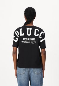 Zwarte katoenen T-shirt met gedurfde witte tekst "COLUCCI ESTABLISHED Milano 1978" op de achterkant, met een relaxte pasvorm en korte mouwen.