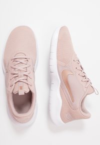 Paire de baskets Nike rose clair avec semelles blanches, tissu tricoté, lacets et logo Nike swoosh sur le côté, présentées sur un fond blanc.