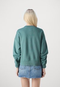 Felpa verde con scollatura rotonda e spalle cadenti, abbinata a una minigonna di jeans con orlo sfilacciato e tasche posteriori.