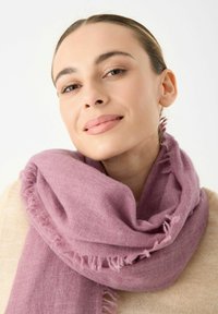 Écharpe frangée rose en tissu doux, drapée autour du cou, avec une texture lisse et une apparence décontractée.