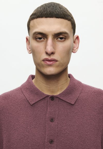 Polo shirt texturat mauve cu guler, având nasturi maro închis și un material moale, pufos. Modelul se află într-o poziție directă față de cameră.