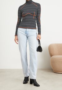 Svart långärmad tröja med geometriskt mönster och orange sömmar, ihopparad med ljusblå raka jeans och svarta klackstövlar.