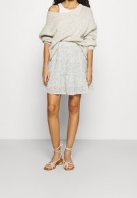 Maglione oversize grigio chiaro lavorato a maglia, gonna con volant floreale pastello e sandali bianchi con cinturino. Vestibilità rilassata con una finitura testurizzata.