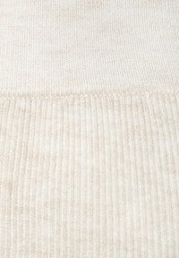 Beige ribbed knit fabric, featuring a soft texture with slight variations in color. Smooth top section transitions to a thicker ribbed pattern below.