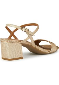 Sandales à talons beiges en matériau texturé, dotées de brides entrecroisées et d'un talon bloc carré. Détail de boucle ajustable à la cheville.